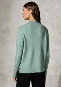 Ljusgrön tröja med ribbade, rundade halsringning och mudd. Har en avslappnad passform och sidofyssar vid fållen för extra komfort.