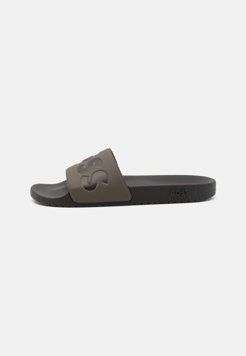Sandal med bred rem i mørketaupe gummi med preget logo; teksturert fotseng og svart såle med skåret kant.
