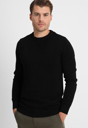 Svart strikket genser med fiskebensmønster, rund hals og ribbede mansjetter. Laget av mykt materiale, designet for en kroppsnær silhuett.