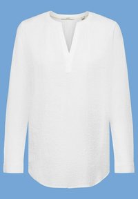 Blouse blanche à manches longues texturée avec un décolleté en V fendu et un ourlet arrondi sur fond bleu.