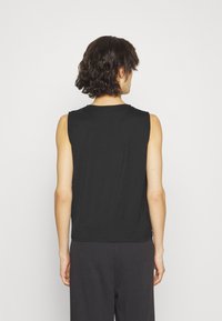 Black sleeveless top with a simple design; round neckline, fitted shape, soft texture, and smooth fabric, paired with dark pants.