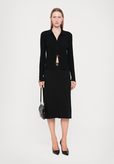 Black ribbed long-sleeve cardigan with buttons, paired with a straight black midi skirt. Accessorized with a black shoulder bag and heels.