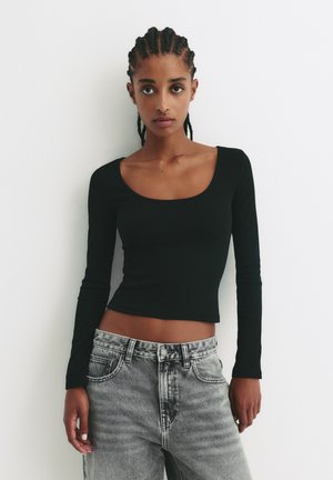 Černá dlouhá rukávová košile s kulatým výstřihem, spárovaná s vysokým pasem, světle šedými džíny z denimu s vybledlou texturou a standardními kapsami.