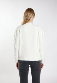 Maglione bianco lavorato a maglia con collo rotondo, maniche testurizzate con un design a treccia e orlo a coste. Abbinato a jeans grigio scuro.