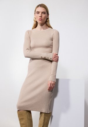 Gestreiftes Strickkleid in Beige mit langen Ärmeln, rundem Ausschnitt und seitlichen Schlitzen. Knopfdetail an den Manschetten. Weiche Textur und figurbetonter Schnitt.