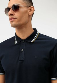 Polo della marina con tessuto testurizzato, due bottoni e accenti a righe nel colletto in bianco e oro. Include un piccolo logo sul petto.