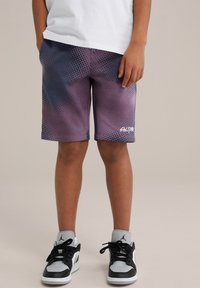 Fialové a námorníčkovské vzorované šortky z mäkkej tkaniny, s voľným strihom a logom na leme. Čierne a šedé tenisky dotvárajú celý vzhľad.