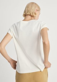 Vit kortärmad T-shirt med rund halsringning, slät textur, lätt passform vid axlarna och en odekorerad baksida.
