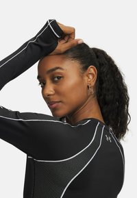 Zwarte sporttop van vochtafvoerende stof, met meshpanelen en witte accenten. Heeft lange mouwen en een ronde halslijn.