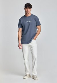 Herrkortärmad blå T-shirt med "POLO CLUB" tryckt i vitt. Kombinerad med vita byxor och ljusa sneakers. Slät tygkvalitet, avslappnad passform.