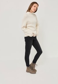 Cream-colored knitted sweater with a high neck, paired with black skinny jeans and brown lace-up ankle boots. Simple design, textured fabric.