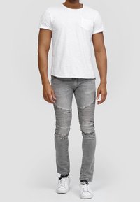 T-shirt bianco a maniche corte con taschino, abbinato a jeans skinny grigi strappati con dettagli a righe orizzontali e sneakers bianche.