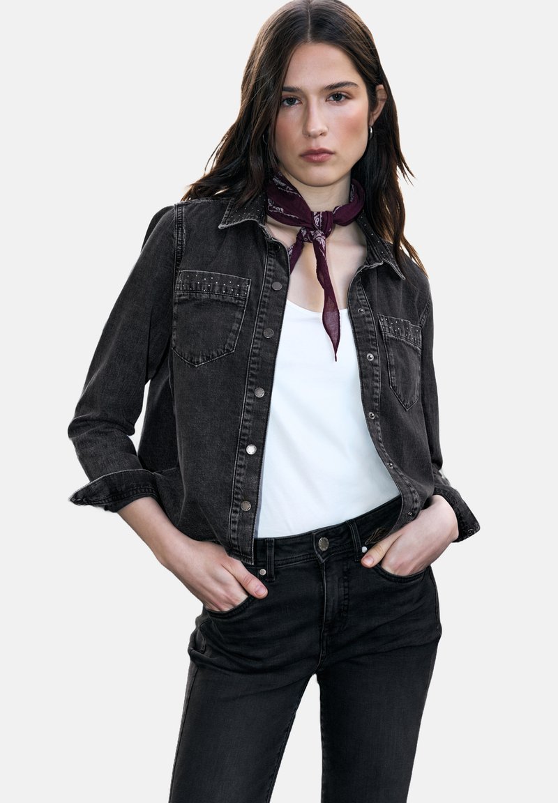 Black denim shirt with button closure, two chest pockets, and studded accents. Paired with a white t-shirt and black jeans. Dark textured fabric.