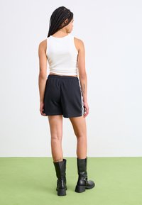 Black shorts with white side stripes, a white fitted tank top, and knee-high black boots. Smooth fabric with elastic waistband.