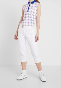 Ärmlös rutig polotröja i vitt med blå detaljer. Vita capribyxor. Vita sportskor fulländar outfiten. Enkel, funktionell design.