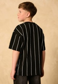 T-shirt nera a maniche corte con strisce verticali bianche, scollo rotondo e vestibilità comoda, vista da dietro.