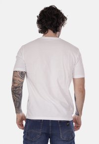 T-shirt bianco in cotone con maniche corte, colletto rotondo e vestibilità comoda. Presenta cuciture minime e un'etichetta sul lato inferiore.