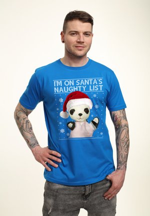 Blå t-shirt med korte ærmer, der har en panda iført en rød julesok, trykt tekst "JEG ER PÅ SANTAS UHELDIGE LISTE" og snefnugdesigns.