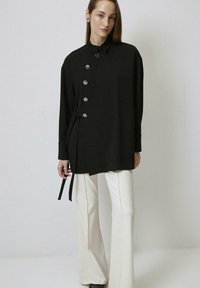 Zwarte long sleeve shirt met kraag, zes grote knopen en zijstrikdetail. Gepaard met crèmekleurige flaredbroek en zwarte schoenen.