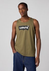 Alyvuogių spalvos medvilninė liemenėlė su apvaliu iškirpimu, kuriame yra didelis juodas Levi's logotipas priekyje ir tiesus kirpimas.