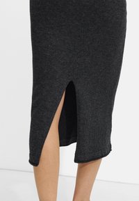 Szara dzianinowa spódnica z bocznym rozcięciem na krawędzi, o gładkiej fakturze i dopasowanym kroju.