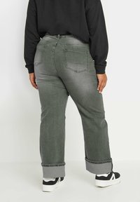 Jeans de mezclilla gris con un corte relajado, que presentan dobladillos enrollados y dos bolsillos traseros. Combinados con zapatillas negras y una camiseta de manga larga negra.