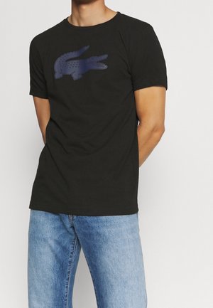 Czarna bawełniana koszulka z nadrukiem ciemnoniebieskiego krokodyla na przodzie. Klasyczny okrągły dekolt i krótkie rękawy, dopasowany krój.