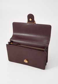 Σακούλα από σκούρο μπορντό δέρμα με κλείσιμο μπροστά, χρυσά εξαρτήματα και θήκη με φερμουάρ. Λείος υφής, μινιμαλιστικός σχεδιασμός με κούμπωμα.