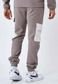 Lichtgrijze joggingbroeken van gestructureerde stof, met witte cargozakken en elastische boorden, gecombineerd met witte Nike sneakers.