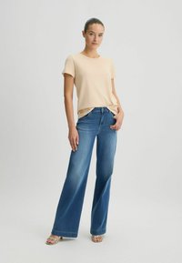 Beige t-shirt met korte mouwen gecombineerd met wijde spijkerbroek in blauw. De outfit heeft een casual pasvorm en lichte stof. De jeans hebben een klassieke wassing.