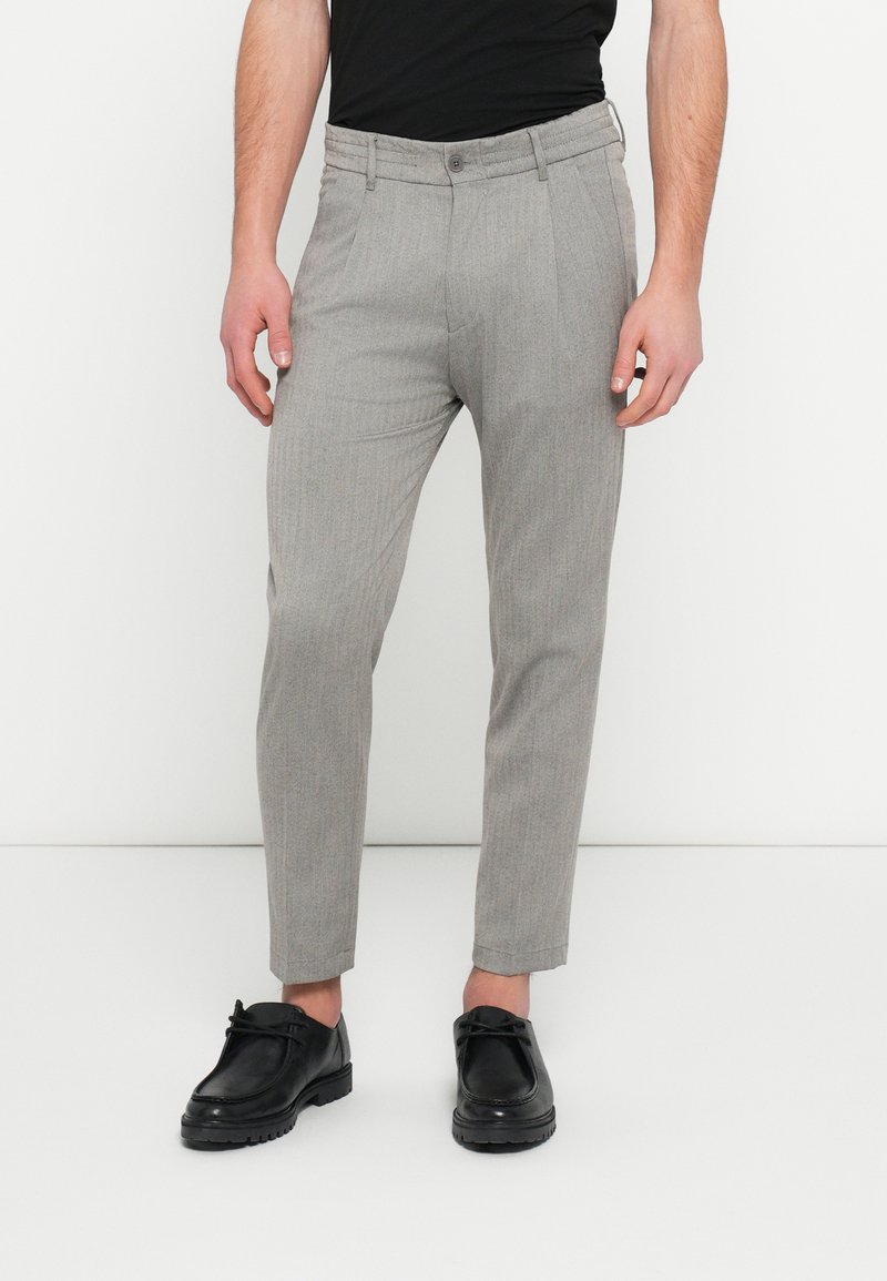 Pantaloni grigi con motivo, a taglio sartoriale e gamba dritta, dotati di chiusura con bottoni e tasche laterali. Indossati con scarpe nere.