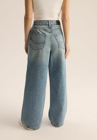 Jasnoniebieskie dżinsy o szerokich nogawkach, z wysokim stanem, dwiema tylkimi kieszeniami i lekkim efektom blaknięcia w dolnej części nogawek.