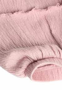 Ljust rosa tyg med en texturerad yta, som har en rynkad manschett med en mjuk, något elastisk kant och fransad fåll.