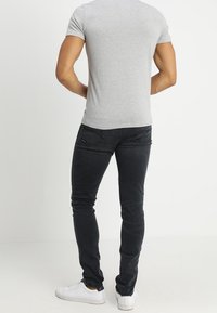 Camiseta gris ajustada, vaqueros negros ajustados con bolsillos traseros, zapatillas blancas lisas. Tejido suave, diseño aerodinámico, acentos de hardware sutiles.
