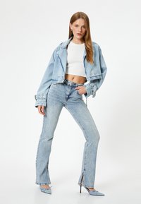 Chaqueta de mezclilla azul claro con diseño cropped y puños enrollados, combinada con jeans azul claro de talle alto que tienen aberturas laterales y una textura ligera.