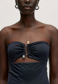 Zwarte strapless zwemoutfit met geplooide stofdetails, een zilveren ringaccent bij het bovenlijfje en een contrasterend doorschijnend uitsnede deel.