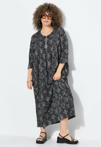 Schwarz-weißer gemusterter Maxikleid mit Rundhalsausschnitt, dreiviertellangen Ärmeln und einem plissierten Design. Kombiniert mit schwarzen Plateausandalen.
