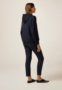 Sweatshirt à capuche bleu marine avec une coupe décontractée, associé à un pantalon slim noir et des chaussures noires à enfiler avec des accents cloutés.