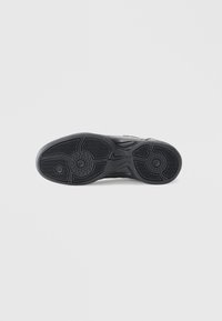 Black athletic shoe sole with textured grip pattern, circular and oval accents, and a distinct Nike logo embedded in the design.