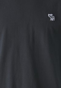 Schwarzes Baumwoll-T-Shirt mit einem kleinen grauen gestickten Elch-Logo auf der linken Seite. Weicher Stoff und klassischer Rundhalsausschnitt.