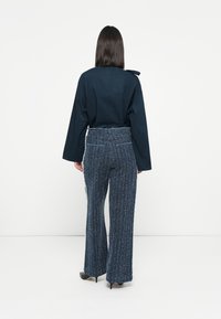 Navy blue blouse with a tie detail and wide, textured blue pants featuring a subtle pattern, paired with black high-heeled shoes.