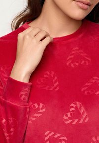 Rød fløjl langærmet top med et præget mønster af hjerter og slikstænger, rund udskæring og tekstureret stof.
