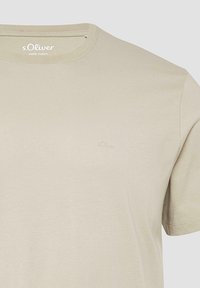 Hellbeige Baumwoll-T-Shirt mit Rundhalsausschnitt und dezent geprägt auf der Brust befindlichem s.Oliver-Logo. Kurze Ärmel mit einer glatten Textur.
