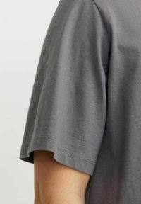 Camiseta de manga corta gris hecha de algodón suave, con cuello redondo y un dobladillo recto con detalles de costura sutiles.