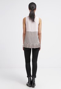 Ärmlös topp med en ljusrosa texturerad överdel och en mönstrad nedre del i brunt och krämfärg, med en volangkant. Kombinerad med svarta skinny jeans.