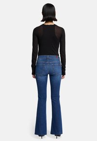 Czarna bluzka z długim rękawem oraz niebieskie dżinsy z szerokimi nogawkami i wysokim stanem, z dżinsowej tekstury, dwoma tylnymi kieszeniami oraz postrzępionym wykończeniem.
