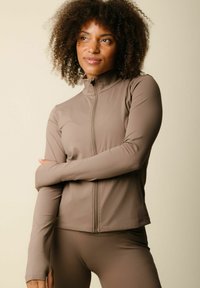 Jachetă cu mâneci lungi și fermoar, în nuanță de taupe, fabricată dintr-un material neted și elastic, cu un design ajustat. Dispune de un guler înalt și mâneci lungi.