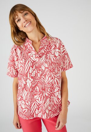 Bluse mit Blumenmuster in rot und weiß, mit V-Ausschnitt und lockerer Passform, kombiniert mit passenden rosa Hosen.