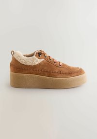 Brown suede sneaker with fluffy cream collar, round laces with red accents, and a thick, textured translucent sole. Side view displayed.