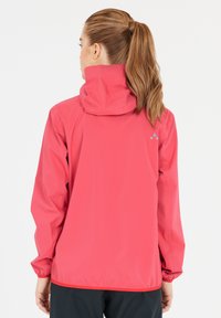 Röd vattentät jacka med huva, elastiska muddar och en figursydd design. Har en logotyp tryckt på baksidan och en slät, blank yta.